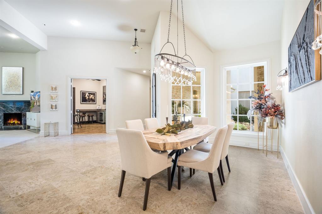Open-concept dining area featuring vaulted ceilings, oversized grid-pane windows, stone tile flooring, a tiered crystal chandelier, and a fireplace with a stone-surround mantle