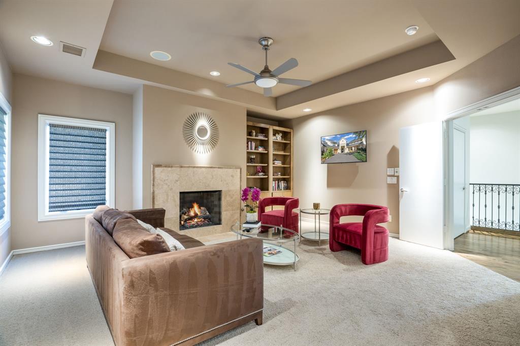 Tray ceiling with recessed lighting, stone-surround fireplace, and built-in wooden shelving