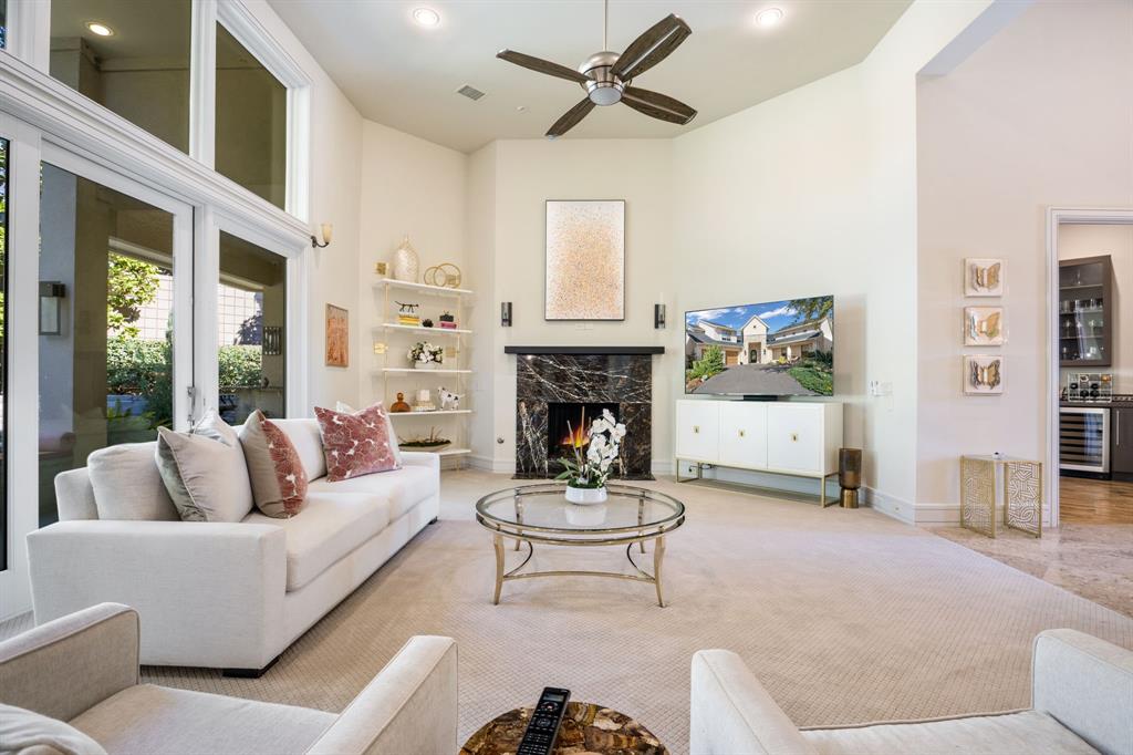 Vaulted ceilings, floor-to-ceiling windows, stone fireplace surround, built-in recessed shelving, and a ceiling fan