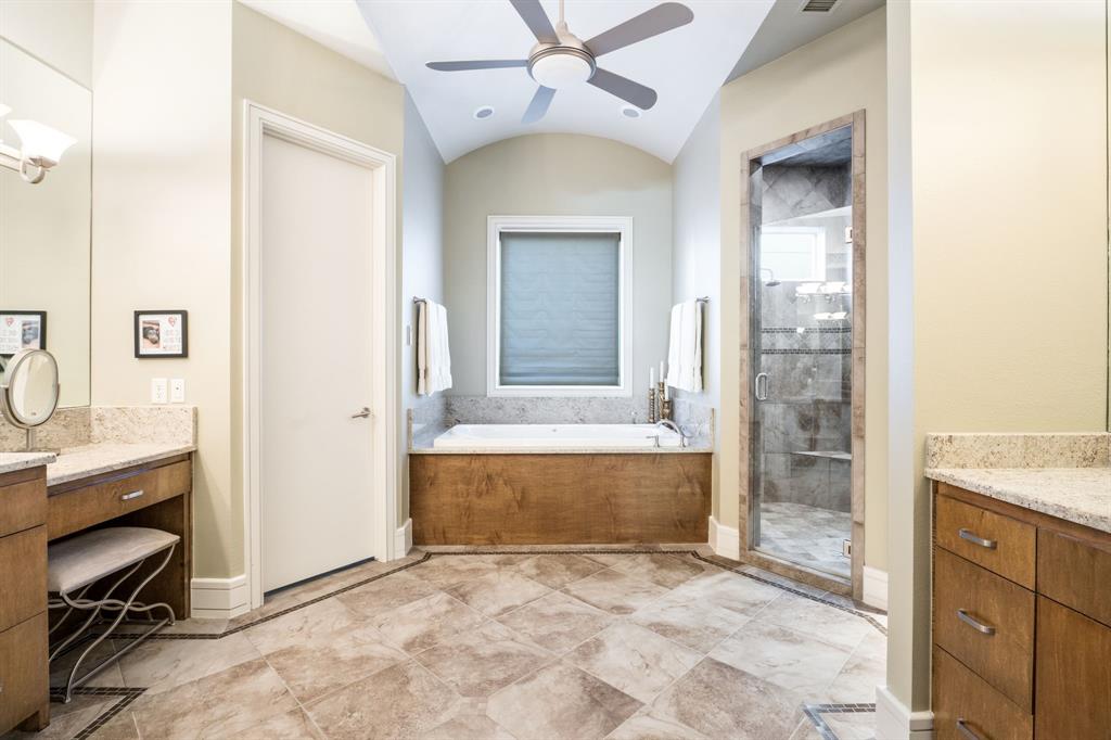 Bathroom featuring a vaulted ceiling with a central fan, stone-tile flooring, a built-in jetted tub with a wood-finish surround, custom wood-finish cabinetry, and a glass-enclosed shower with tiled walls