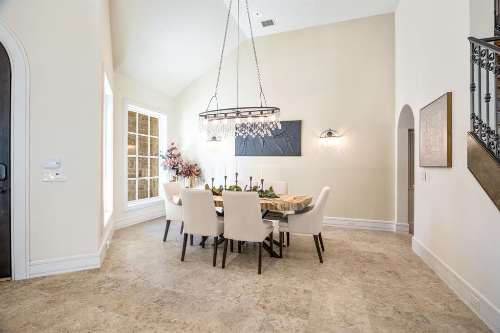 Vaulted ceilings, large-format stone flooring, multi-light crystal chandelier, arched architectural entryways, and wrought iron stair railing