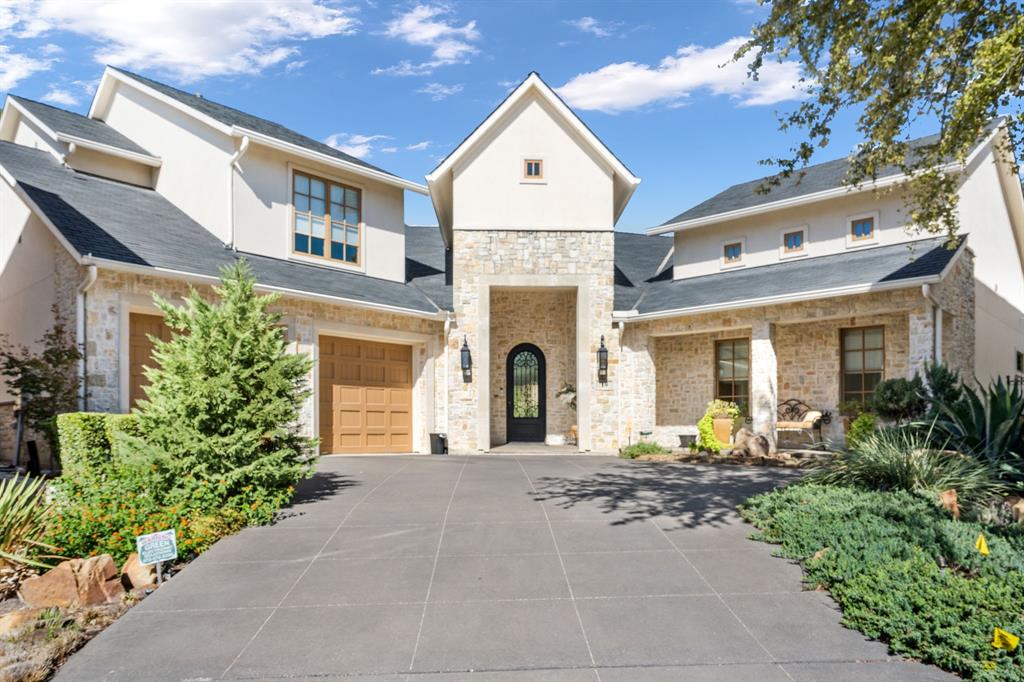 Multi-gabled exterior featuring stone masonry, stucco facade, arched entryway with wrought iron door, and paved driveway