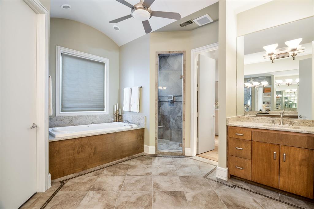 Bathroom featuring a soaking tub with wood-finish cabinetry, a walk-in glass-enclosed shower with tile surround, a single vanity with stone countertop, and tile flooring