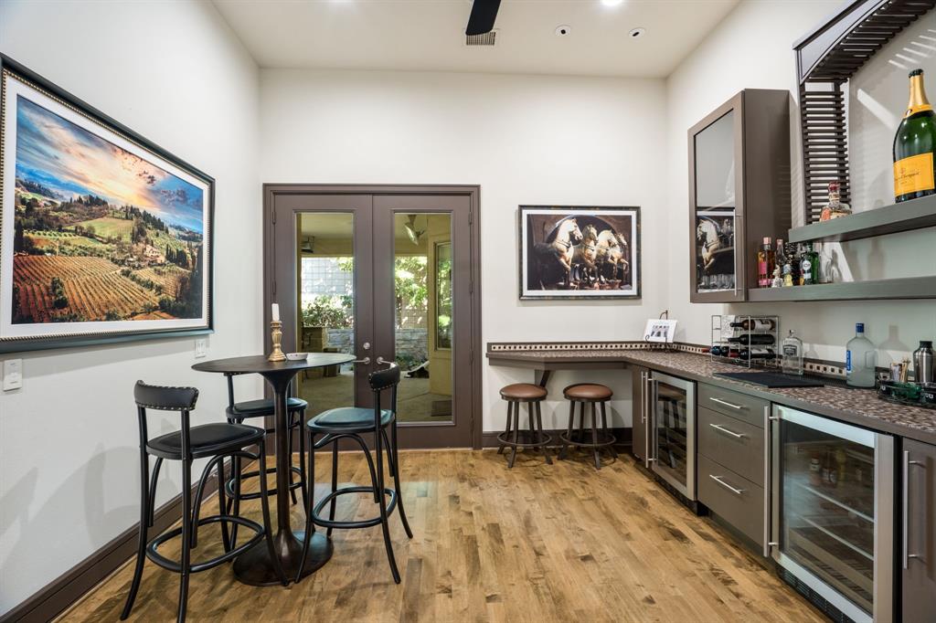 Built-in wet bar featuring stone-finish countertops, glass-front cabinetry, two under-counter beverage refrigerators, wood-finish flooring, and double glass-paned doors