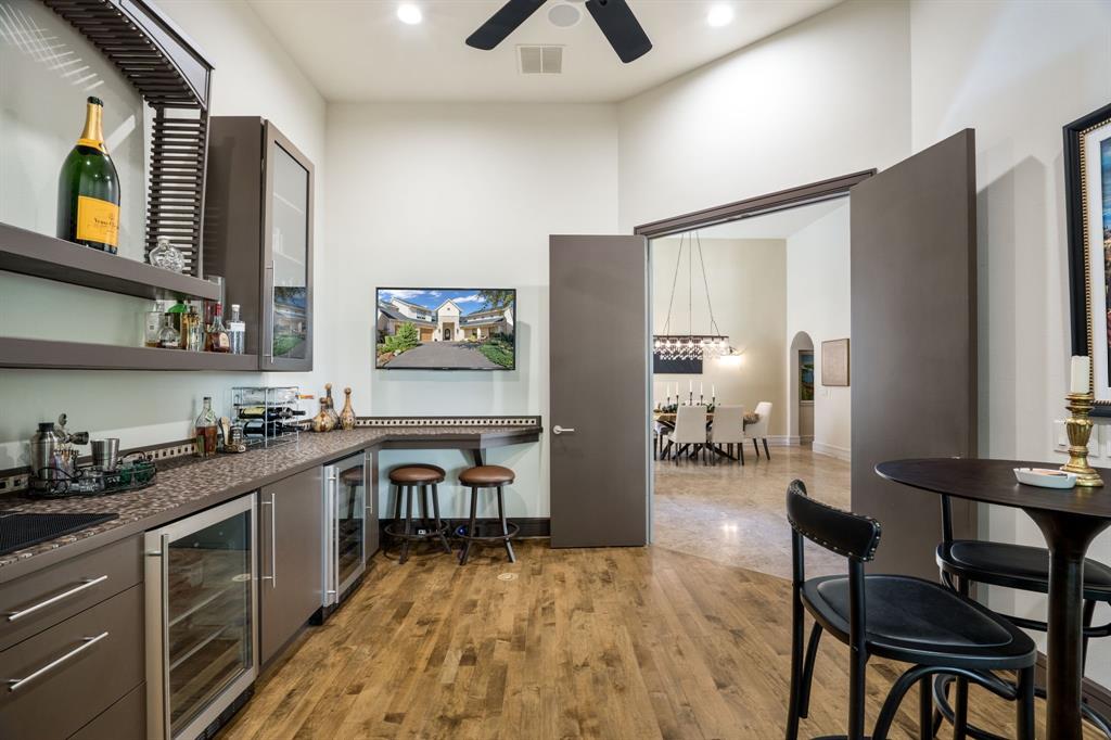 Built-in bar featuring wood-finish flooring, custom cabinetry with glass-front display, integrated beverage refrigeration, and a stone-surface countertop