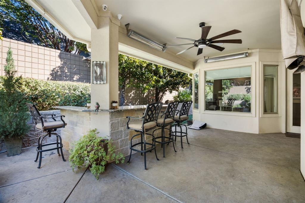 Covered outdoor patio featuring a stone-clad built-in bar, ceiling-mounted heaters, a multi-blade ceiling fan, and concrete flooring