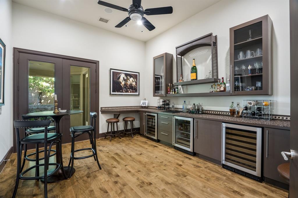 Custom wet bar featuring solid-surface countertops, built-in dual-zone wine refrigeration, glass-front cabinetry, wood-finish flooring, and French door access