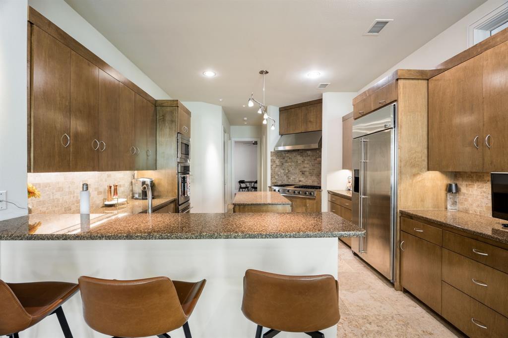 Kitchen featuring wood cabinetry, stone countertops, stone tile backsplash, stainless steel appliances, and recessed lighting