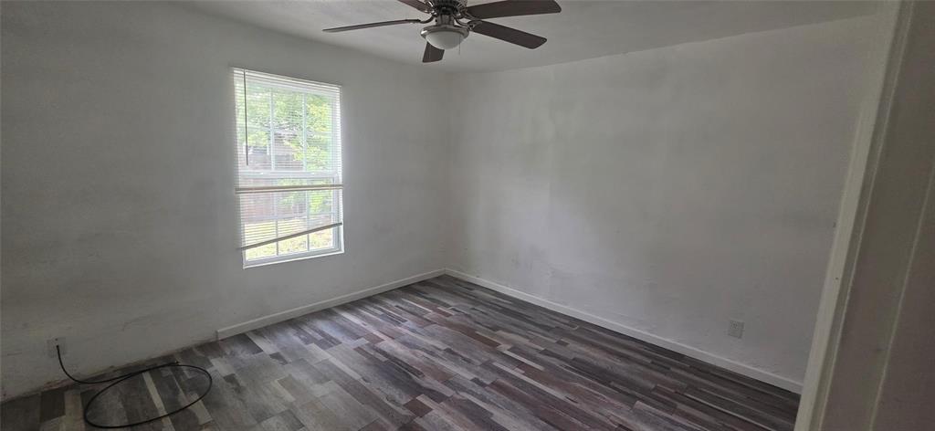 Room featuring wood-finish flooring, neutral wall paint, and a ceiling fan with integrated lighting, completed by a multi-pane window