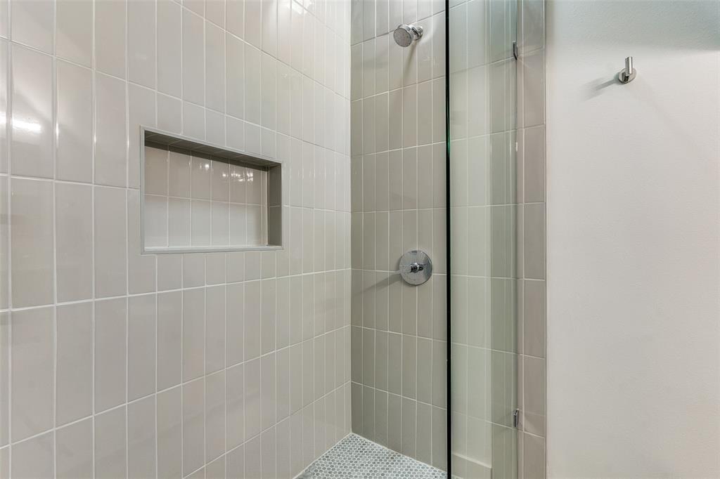 Walk-in shower featuring vertical subway wall tiling, a glass partition, a built-in recessed wall niche, a circular chrome shower head, and a chrome single-handle pressure balance valve