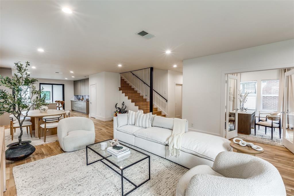 Open-concept floor plan featuring wood-finish flooring, recessed lighting, a staircase with metal railings, and double glass-paned doors