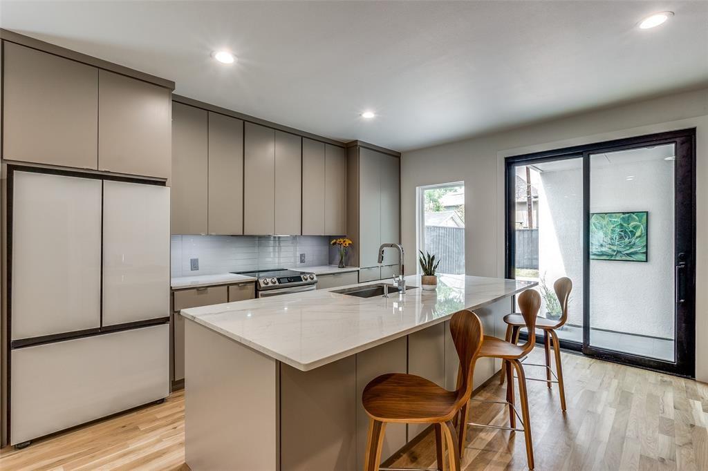 Kitchen featuring flat-panel cabinetry, a central island with a stone-finish countertop, stainless steel undermount sink, integrated refrigerator, and wood-finish flooring