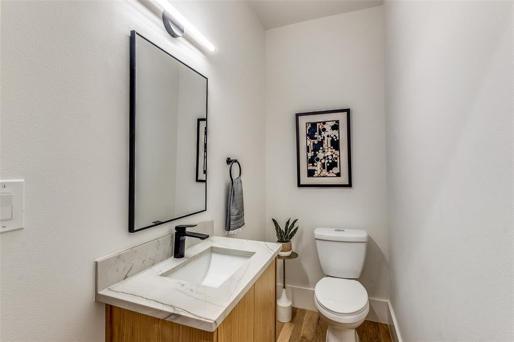 Modern vanity featuring a stone-look countertop, integrated rectangular sink, matte black faucet, minimalist wall-mounted mirror, and wood-finish flooring