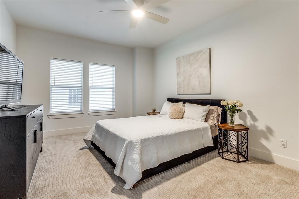 Neutral-toned room featuring plush carpeting, dual windows with horizontal blinds, and a ceiling-mounted fan with integrated lighting