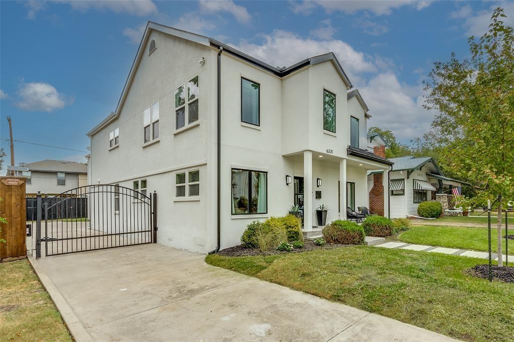 Two-story stucco exterior featuring a covered front porch, dark-framed windows, a concrete driveway, and a gated side entrance