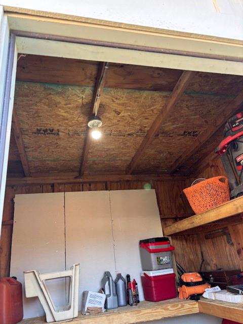 Storage structure featuring exposed wood framing, built-in wooden shelving, and a ceiling-mounted light fixture