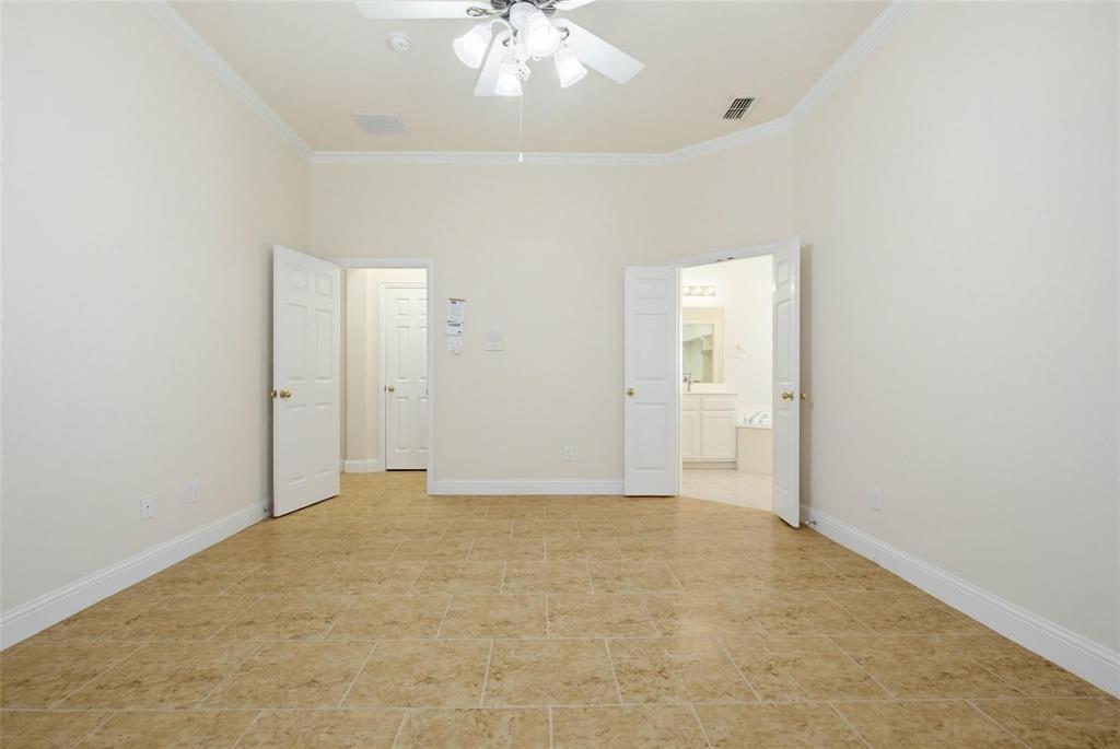 Neutral-toned ceramic tile flooring, vaulted ceilings with crown molding, and a central ceiling fan with multi-light fixture