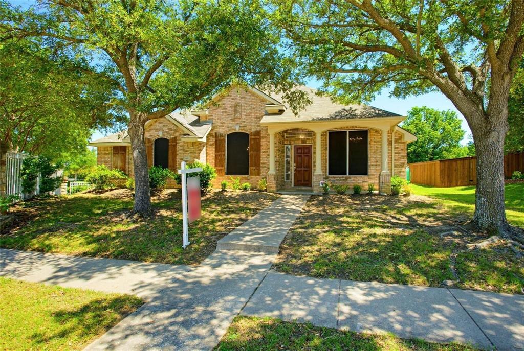Single-story brick exterior featuring a covered front porch, arched window detailing, wood-finish shutters, and mature trees Single-story brick exterior featuring a covered front porch, arched window detailing, wood-finish shutters, and mature trees