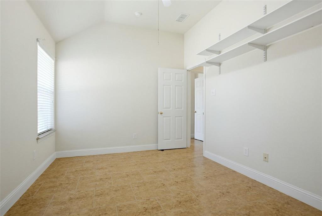 Room featuring a vaulted ceiling, neutral-toned tile flooring, and two tiers of wall-mounted shelving Room featuring a vaulted ceiling, neutral-toned tile flooring, and two tiers of wall-mounted shelving