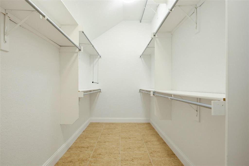 Walk-in closet featuring dual-sided built-in shelving, adjustable metal clothing rods, and tile flooring Walk-in closet featuring dual-sided built-in shelving, adjustable metal clothing rods, and tile flooring