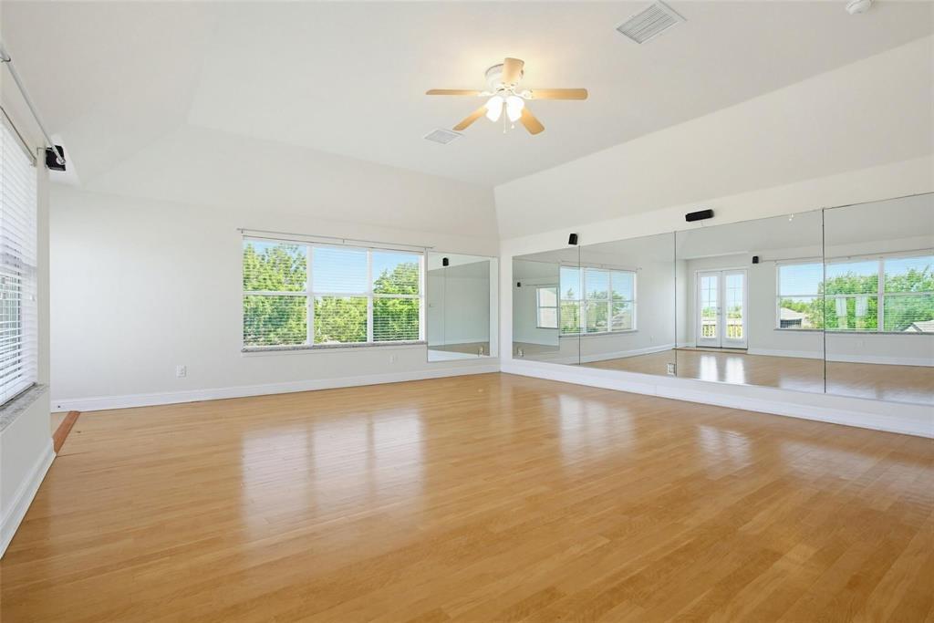 Expansive room featuring vaulted ceilings, wood-finish flooring, floor-to-ceiling wall mirrors, large windows, and a ceiling-mounted light fixture Expansive room featuring vaulted ceilings, wood-finish flooring, floor-to-ceiling wall mirrors, large windows, and a ceiling-mounted light fixture