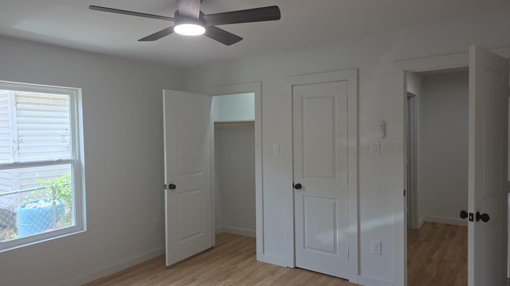 Neutral interior space featuring wood-finish flooring, a ceiling fan with integrated lighting, multi-panel doors, and a reach-in closet with built-in shelving