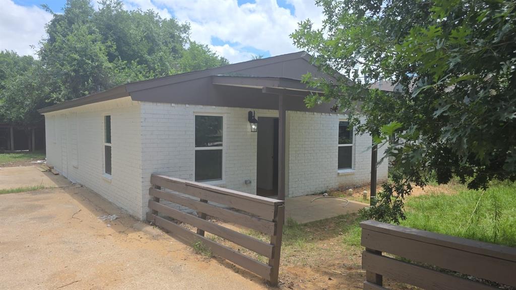 Single-story residence featuring white painted brick exterior, dark-toned trim, front porch, and horizontal wood fencing