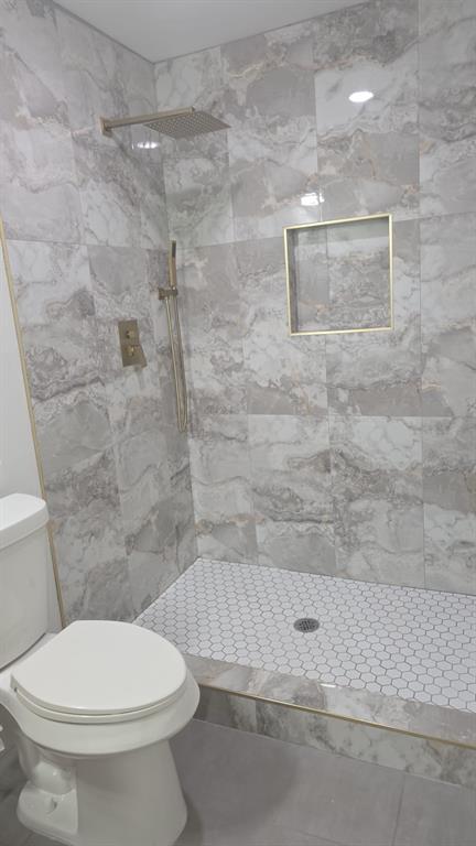 Walk-in shower featuring large-format patterned wall tile, white hexagonal floor tile, recessed wall niche, rainfall showerhead, and gold-finish fixtures