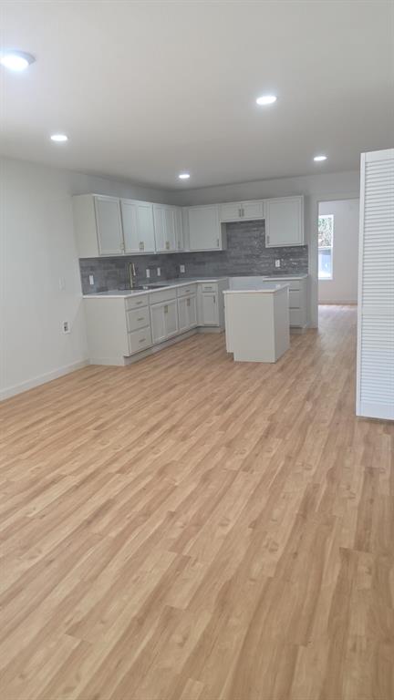 Kitchen featuring white cabinetry, an island, light-toned wood-finish flooring, recessed lighting, and a stone-tile backsplash