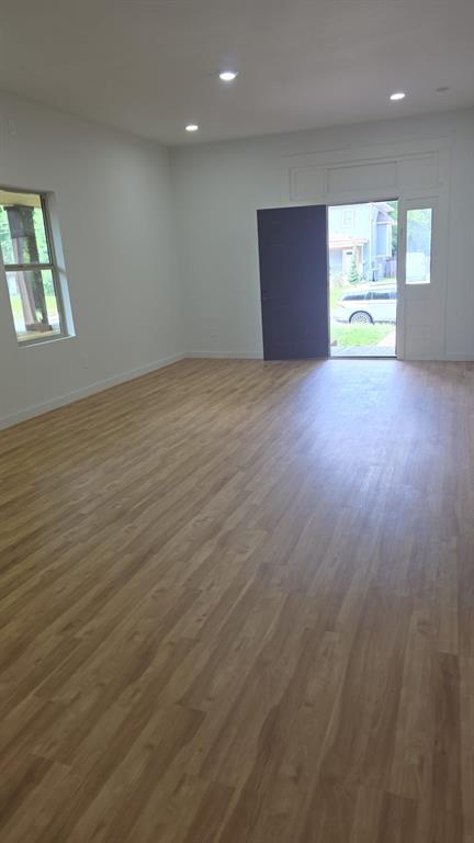 Open-concept interior featuring light wood-finish flooring, recessed lighting, white walls, and an exterior door with a sidelight window