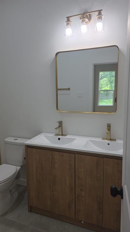 Double-sink vanity with wood-finish cabinetry, metal-finish hardware, rectangular mirror with rounded corners, and three-light glass fixture
