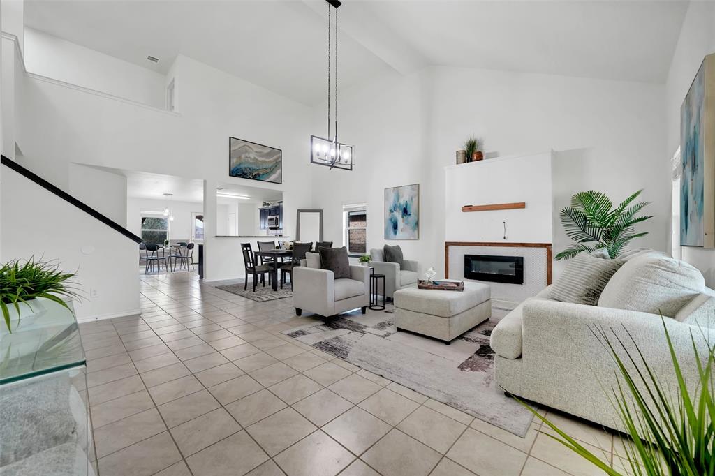 Living area with baseboards, high vaulted ceiling, an inviting chandelier, light tile patterned flooring, and a glass covered fireplace