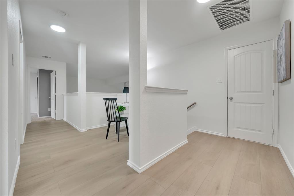 Corridor with light wood-type flooring, visible vents, an upstairs landing, and baseboards