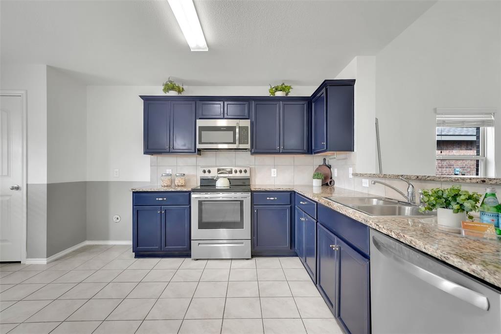 Kitchen featuring a sink, blue cabinetry, appliances with stainless steel finishes, light tile patterned flooring, and decorative backsplash