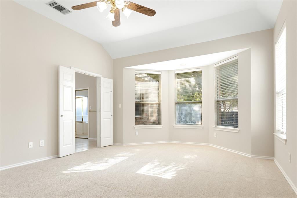 Vaulted ceilings featuring a central ceiling fan with integrated lighting, expansive bay window, and neutral wall-to-wall carpeting