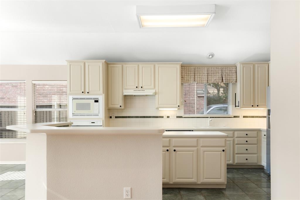 Kitchen featuring off-white cabinetry, solid surface countertops, tile backsplash, built-in microwave, and tile flooring