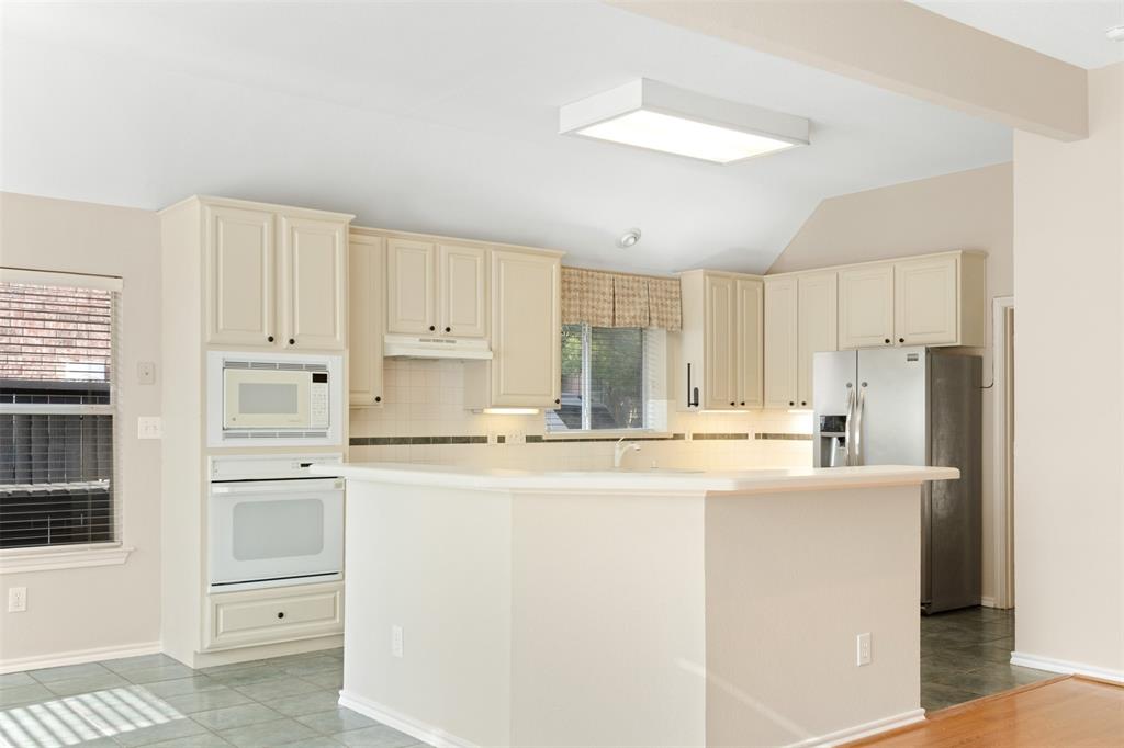 Kitchen featuring cream-colored cabinetry, a peninsula countertop, built-in wall oven and microwave, stainless steel refrigerator, and tiled flooring