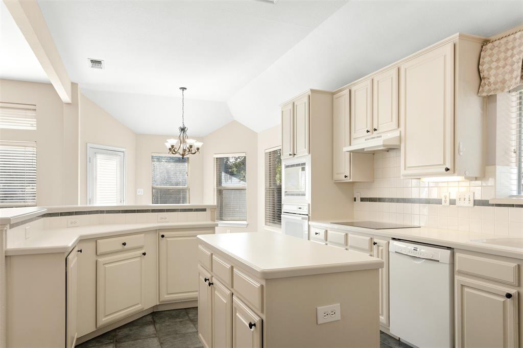 Kitchen featuring off-white cabinetry, central island, integrated wall oven, tile backsplash with decorative inlay, and vaulted ceiling