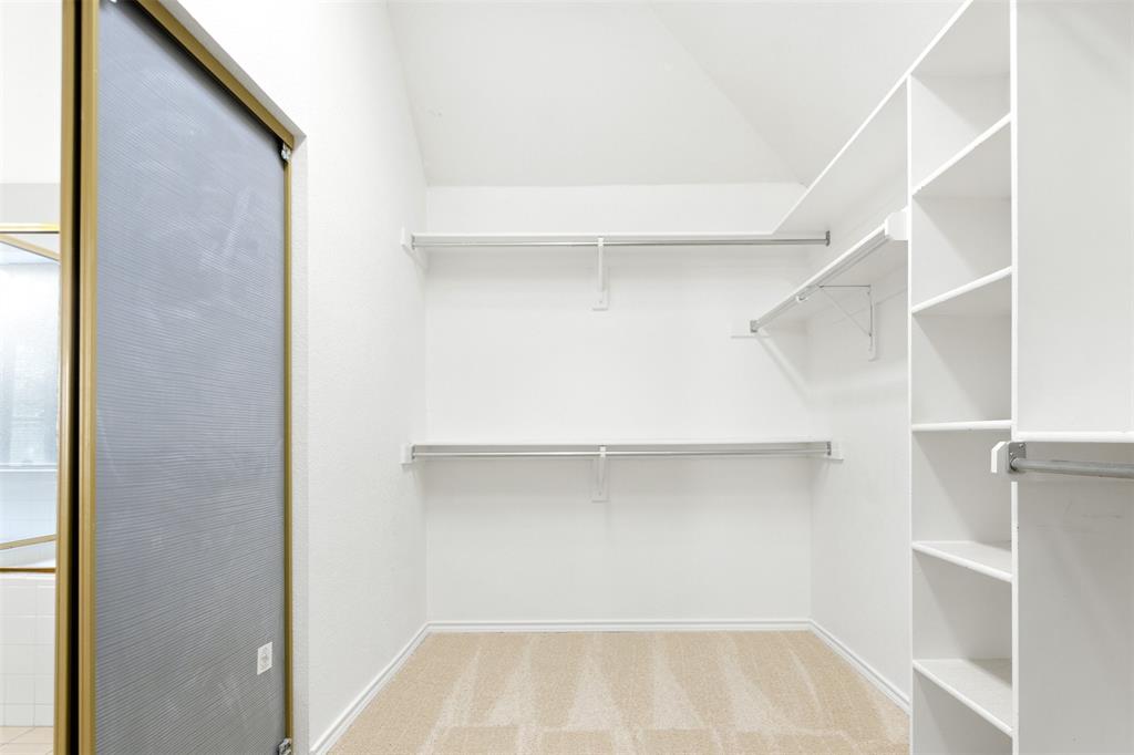 Walk-in closet featuring vaulted ceilings, floor-to-ceiling built-in shelving, dual-level metal hanging rods, and neutral carpeting