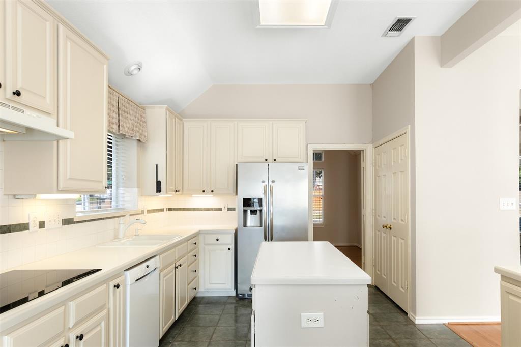 Kitchen featuring off-white cabinetry, solid surface countertops, tiled backsplash with decorative inlay, stainless steel refrigerator, and tiled flooring