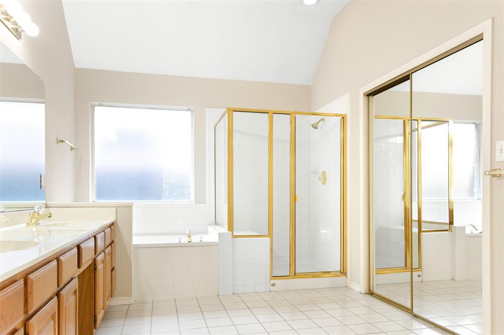 Bathroom featuring a vaulted ceiling, soaking tub, glass-enclosed shower with metal framing, vanity with wooden cabinetry, and sliding mirrored wardrobe doors