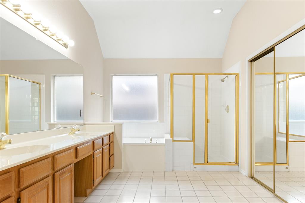 Bathroom featuring a dual-sink vanity, tiled floor, glass-enclosed shower, soaking tub, and vaulted ceiling