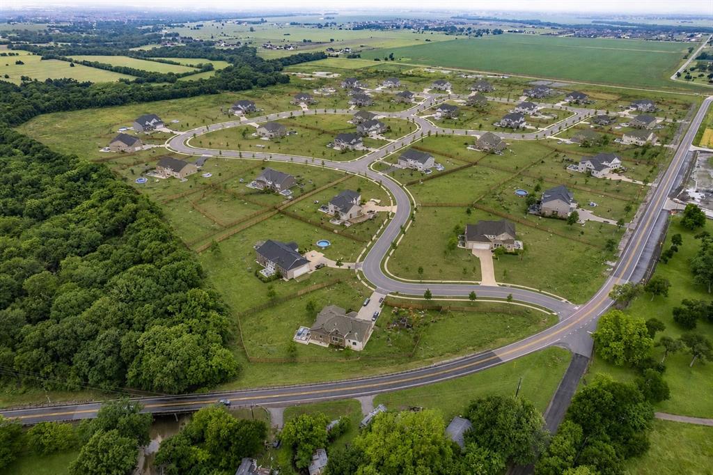 Aerial perspective of a residential community featuring winding paved roads, expansive open green space, mature wooded borders, and individual detached dwellings Aerial perspective of a residential community featuring winding paved roads, expansive open green space, mature wooded borders, and individual detached dwellings