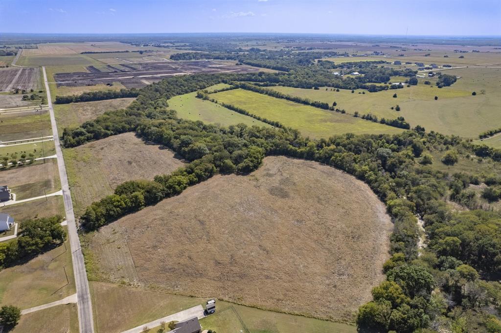 Aerial perspective of expansive acreage featuring open cleared fields, mature tree lines, and paved road access Aerial perspective of expansive acreage featuring open cleared fields, mature tree lines, and paved road access