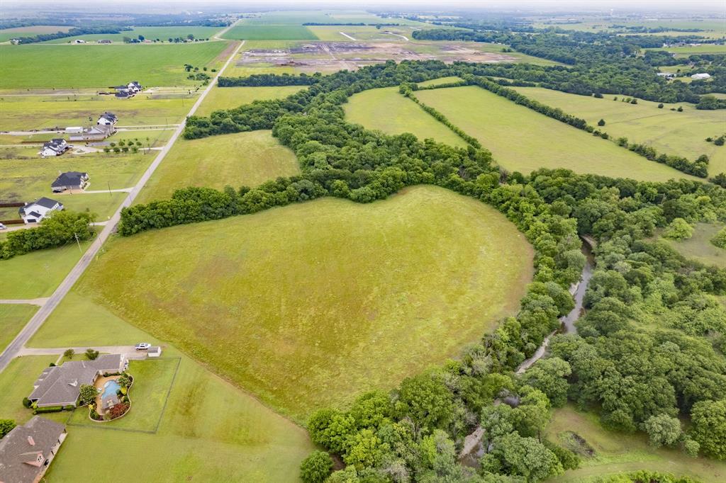 Aerial perspective of expansive acreage featuring open pasture, mature tree clusters, and a natural creek boundary Aerial perspective of expansive acreage featuring open pasture, mature tree clusters, and a natural creek boundary