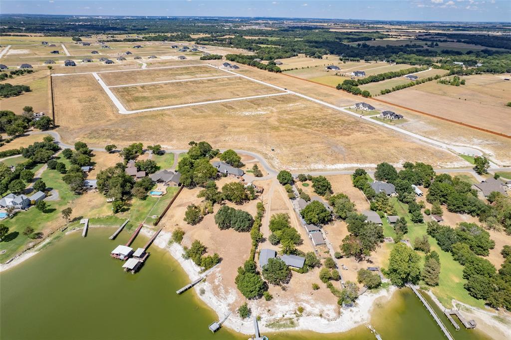 Aerial perspective of expansive acreage featuring waterfront access, private boat docks, mature tree clusters, and paved road frontage