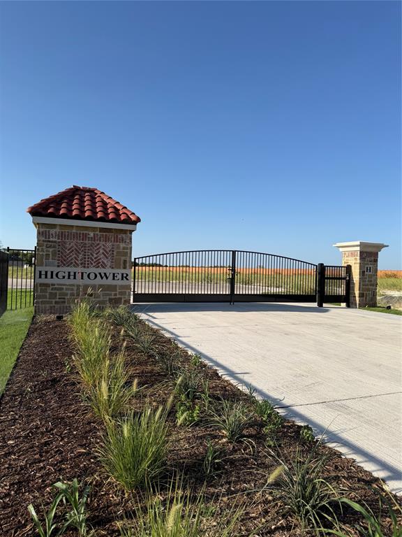 Gated entry featuring a concrete driveway, metal security gate, and stone-clad pillars with red tile caps