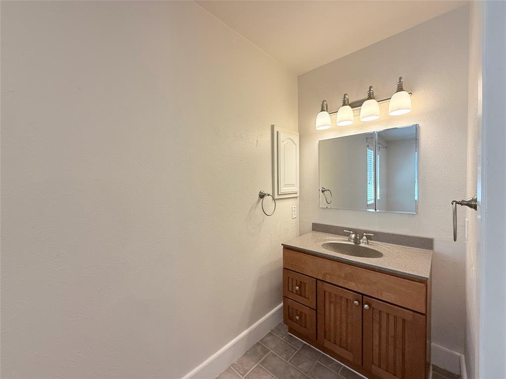 Vanity featuring wood-finish cabinetry, a stone-composite countertop with an integrated oval sink, a tri-fold medicine cabinet, and a four-light polished chrome fixture over tile flooring