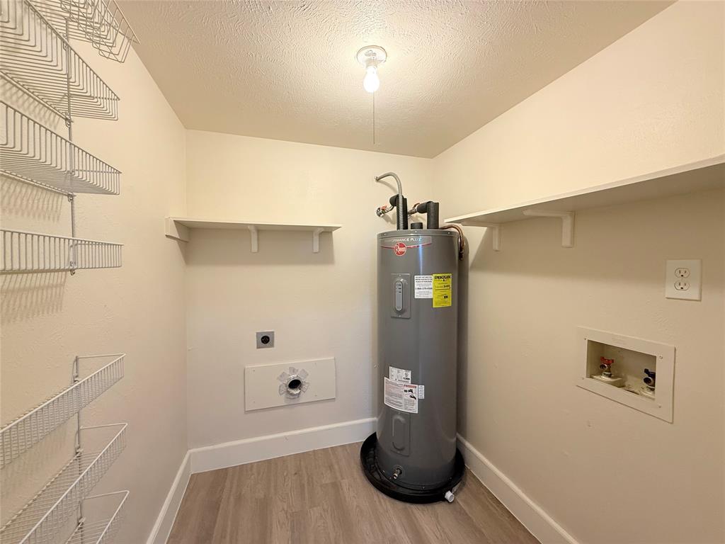 Utility room featuring wood-finish flooring, wall-mounted metal wire shelving, fixed upper shelving, and a water heater