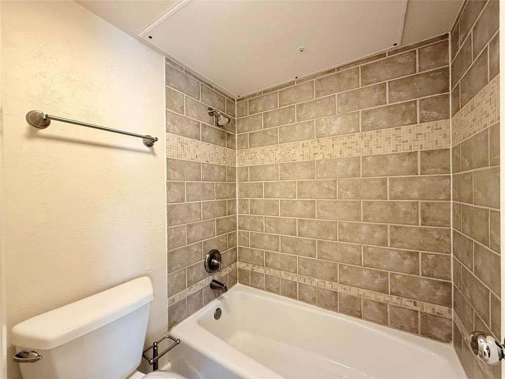 Bathtub with a white surround, integrated shower fixture, and tiled walls featuring a decorative mosaic border inlay